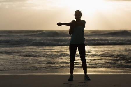 Sporty brunette stretching on the beach in the evening