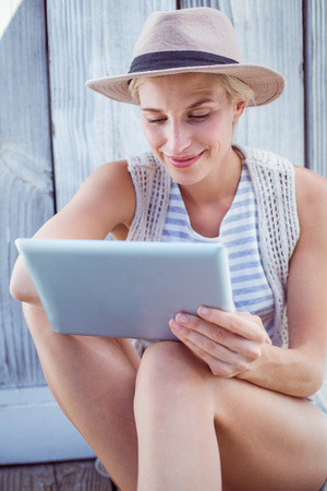 Pretty blonde woman using her tablet on wooden backgroundの写真素材
