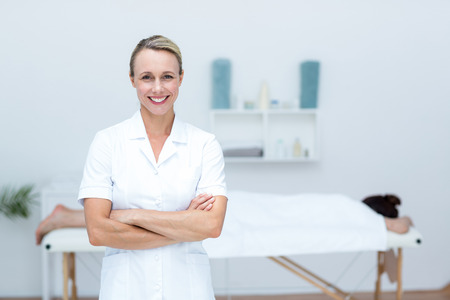 Physiotherapist smiling at camera arms crossed in medical officeの写真素材