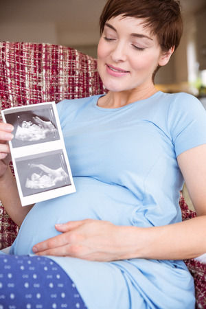 Pregnant woman looking at ultrasound scans at home in the living roomの写真素材