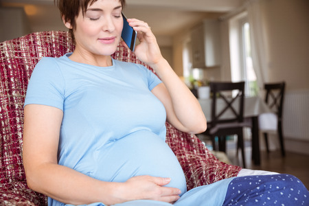 Pregnant woman making a call at home in the living roomの写真素材