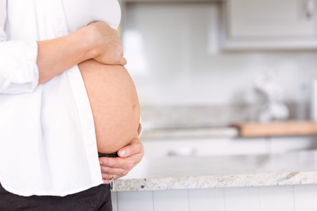 Pregnant woman holding her bump at home in the kitchen