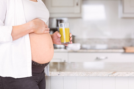 Pregnant woman drinking glass of orange juice at home in the kitchenの写真素材