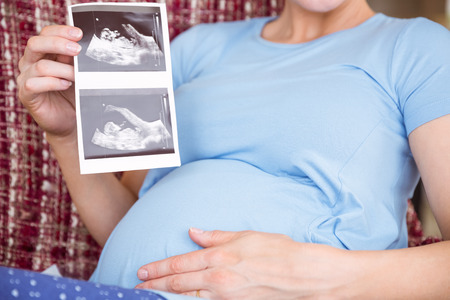 Pregnant woman looking at ultrasound scans at home in the living roomの写真素材