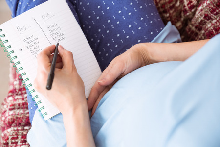 Pregnant woman listing baby names at home in the living roomの写真素材