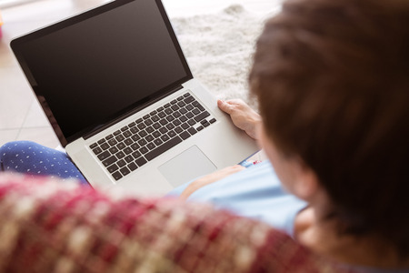 Pregnant woman using her laptop at home in the living roomの写真素材