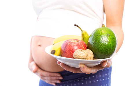 Pregnant woman showing fruit and veg on white backgroundの写真素材