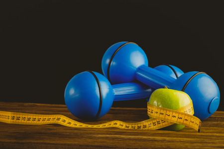 Blue dumbbells with green apple and measuring tape on wooden backgroundの写真素材