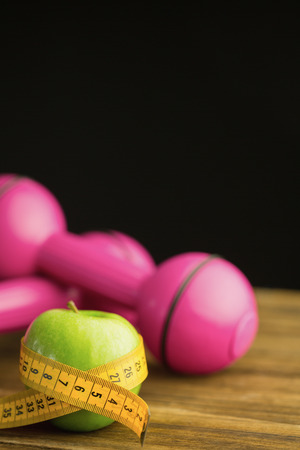 Pink dumbbells with green apple and measuring tape on wooden backgroundの写真素材