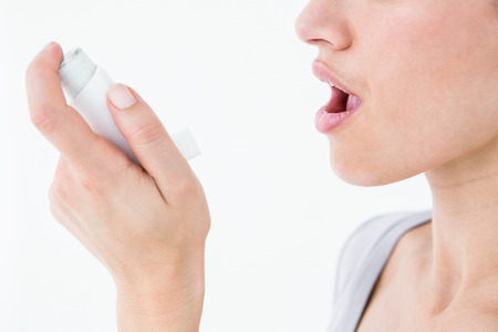 Asthmatic pretty brunette using inhaler on white backgroundの写真素材