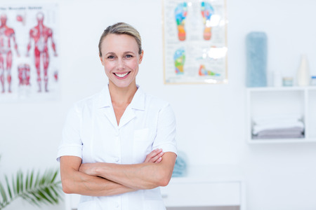 Smiling doctor looking at camera with arms crossed in medical officeの写真素材
