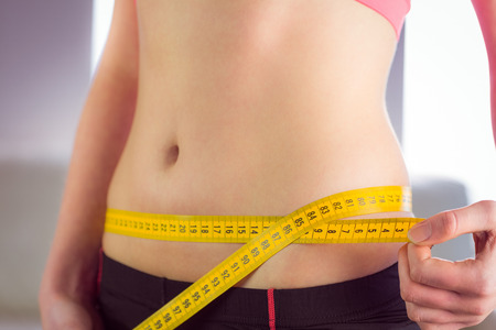 Slim woman measuring waist with tape measure at home in the living-room