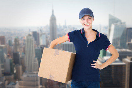 Happy delivery woman holding cardboard box  against new yorkの写真素材