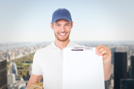 Happy delivery man holding cardboard box and clipboard against new yorkの写真素材