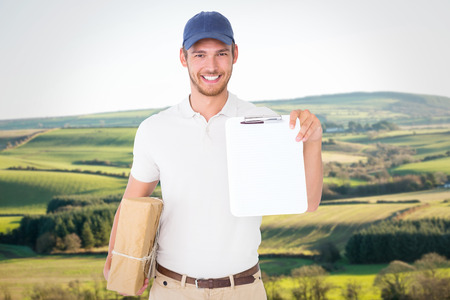 Happy delivery man holding cardboard box and clipboard against scenic landscape