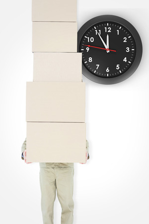 Delivery man carrying stacked boxes against clockの写真素材
