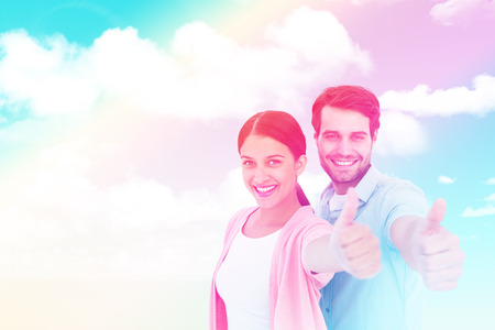 Happy couple showing thumbs up against blue skyの写真素材