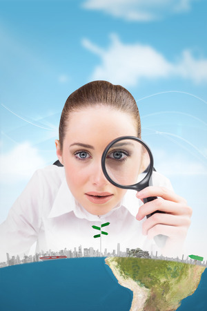 Businesswoman typing and looking through magnifying glass against blue skyの写真素材