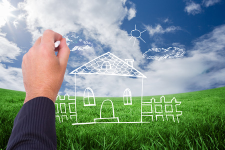 Hand of a businessman writing with a chalk against green field under blue skyの写真素材