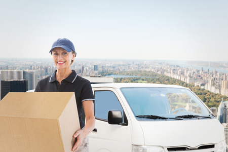 Happy delivery woman holding cardboard box against new yorkの写真素材