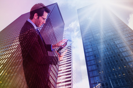 Businessman standing while using a tablet pc against low angle view of skyscrapersの写真素材