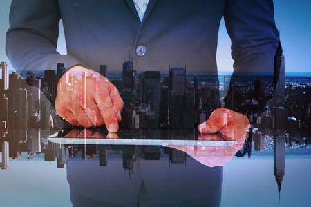 Businessman using his tablet pc  against mirror image of city skylineの写真素材