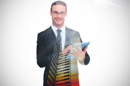 Happy businessman using his tablet pc  against low angle view of skyscrapers at sunsetの写真素材