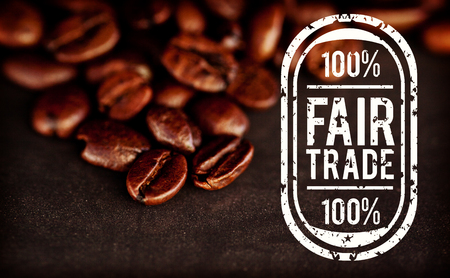 Fair Trade graphic against dark blurred coffee seeds laid out together on a black tableの写真素材
