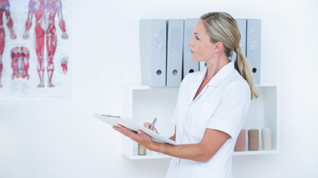 Doctor writing on clipboard in medical officeの写真素材