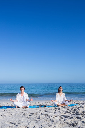 Happy couple doing yoga beside the water at the beachの写真素材