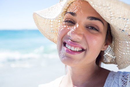 Pretty brunette wearing straw hat and looking at camera at the beachの写真素材