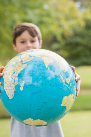 Smiling boy holding an earth globe in the park on a sunny dayの写真素材