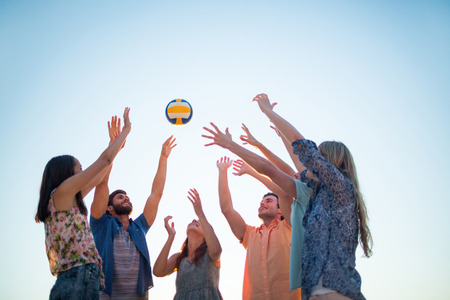 Happy friends throwing volleyball at the beach