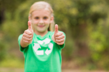 Happy little girl in green with thumbs up on a sunny dayの写真素材