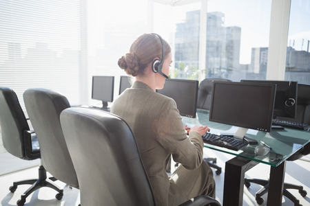 Smiling businesswoman with headset using computers in officeの写真素材