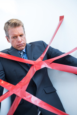 Businessman trapped by red tape on white backgroundの写真素材