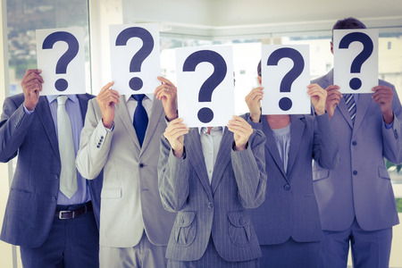 Business team holding question marks over face in the office