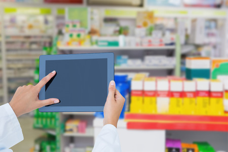 Doctor using tablet pc  against close up of shelves of drugsの写真素材