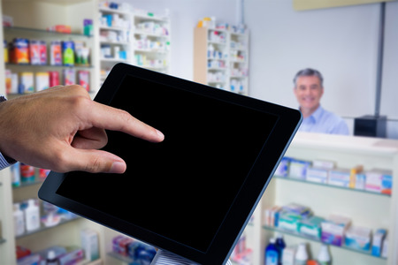 Man using tablet pc  against pharmacist with grey hair standing behind shelves of drugsの写真素材
