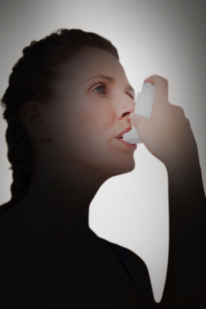 Woman using inhaler for asthma against grey vignetteの写真素材
