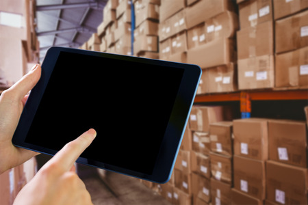 Man using tablet pc against forklift in large warehouse