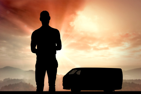 Happy delivery man with cardboard box and clipboard against sun shining over mountainsの写真素材