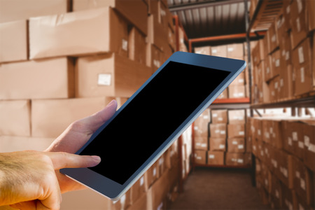 Man using tablet pc against shelves with boxes in warehouse