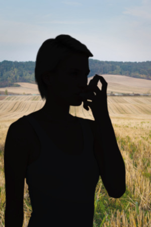 Blonde woman taking her inhaler against rural fields against trees and skyの写真素材