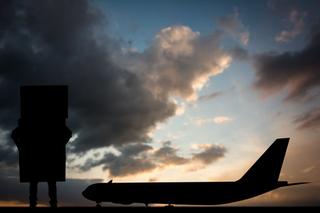 Man carrying pile of boxes against blue and orange sky with cloudsの写真素材
