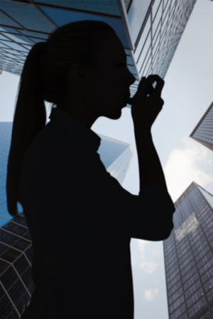 Beautiful blonde using an asthma inhaler against skyscraperの写真素材