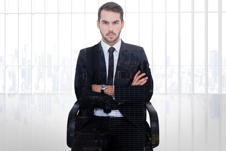 Serious businessman sitting with arms crossed against city skylineの写真素材