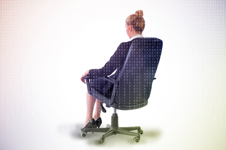 Businesswoman sitting on swivel chair in black suit against digitally generated server room with towersの写真素材