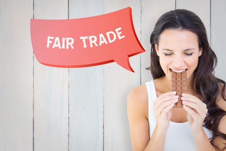 Pretty brunette eating bar of chocolate against wooden planksの写真素材