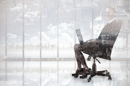 Businesswoman sitting on swivel chair with laptop against new yorkの写真素材